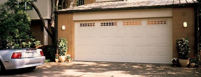 White garage door with a row of windows on a home with a car parked in the driveway