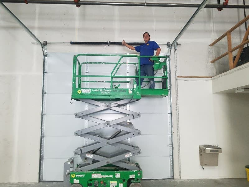 Technician on a scissor lift beside a commercial garage door and its torsion spring