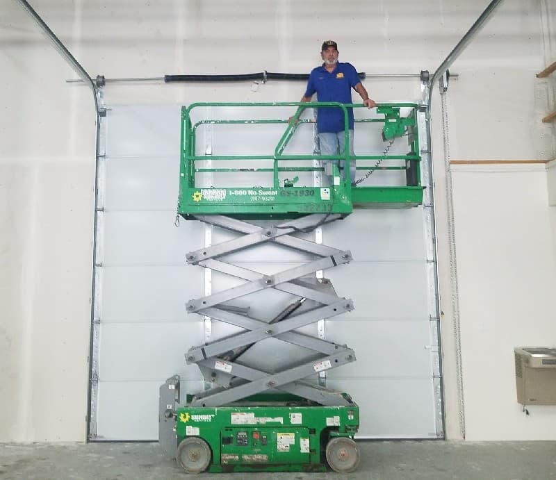 Technician on a scissor lift inspecting the spring above a large commercial garage door