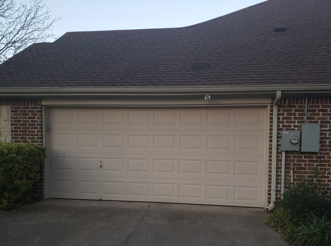 Beige raised-panel two-car garage door on a dark brick home in Granbury, Texas