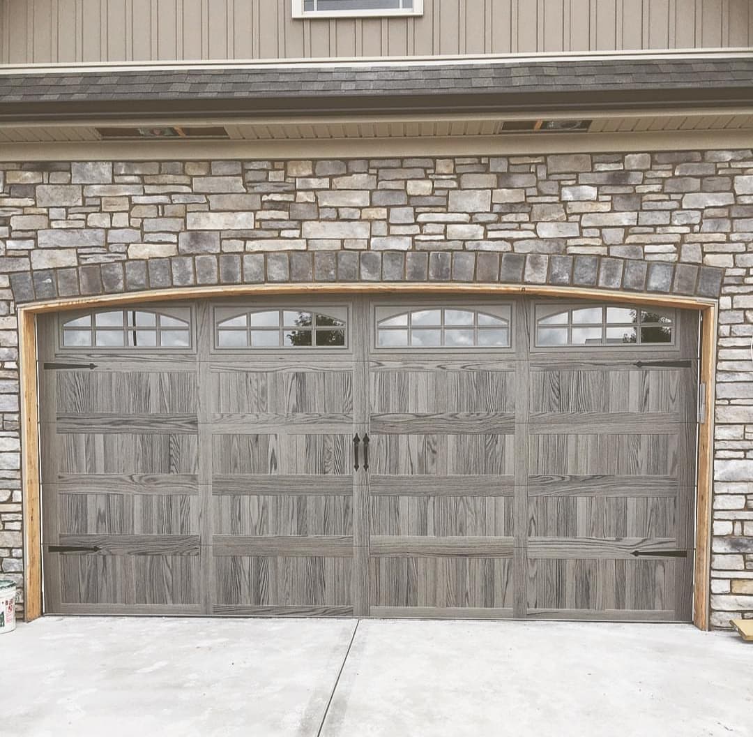 Gray wood-look carriage-style garage door with arched windows under a stone arch